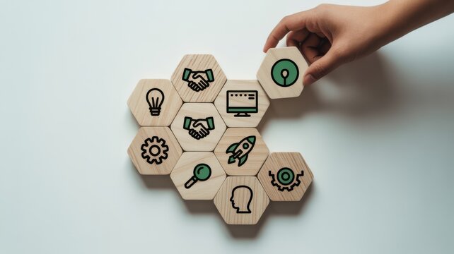 Hand placing green gear icon on wooden hexagon blocks with business symbols