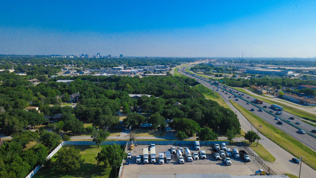 Rows of heavy freight trucks occupy a secure gravel and asphalt depot adjacent to a multi lane roadway. Commercial transport vehicles line up neatly near perimeter fencing, Irving, Texas