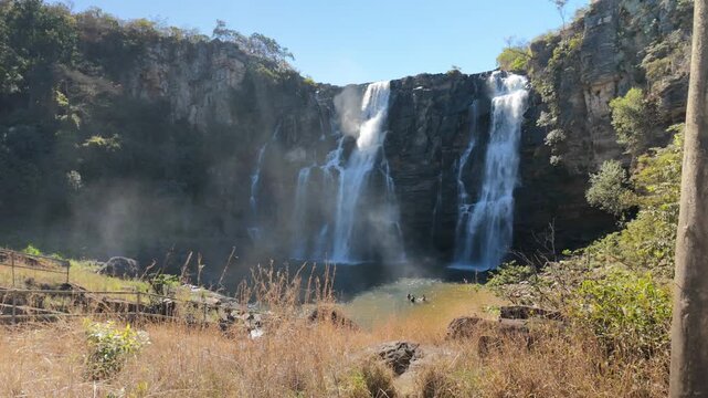 Wide landscape view of Salto Corumba waterfall with tourists swimming in the natural pool during dry season