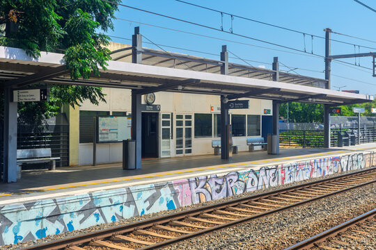 Barcelona, ​​Spain, June 29, 2026. An empty outdoor train station platform with a covered shelter, metal benches, and colorful graffiti on the concrete edge along the railway tracks.