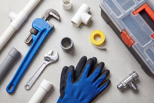 Plumbing tools and pipe fittings flat lay on grey background