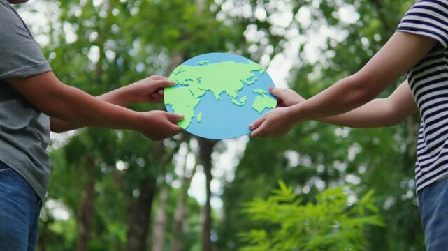 Two people holding a paper earth globe together in a lush green forest. Concept of earth care, eco-friendliness, sustainability, teamwork, and ESG strategy.