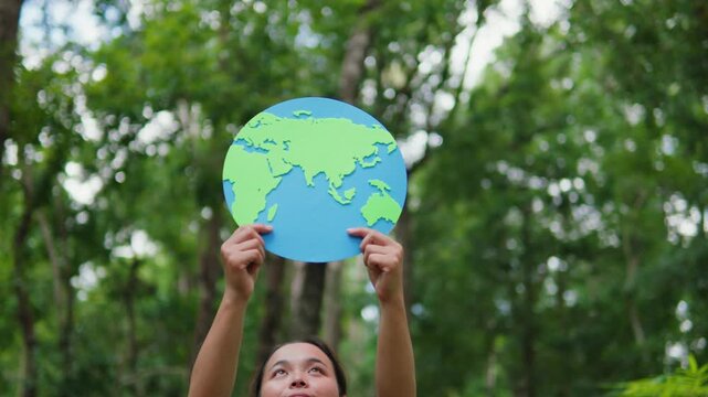 Young woman holding an earth globe in a green forest. Concept of earth care, environmental protection, saving the planet, sustainability, and eco-friendliness.
