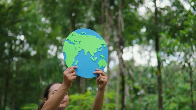 Young woman holding an earth globe in a green forest. Concept of earth care, environmental protection, saving the planet, sustainability, and eco-friendliness.