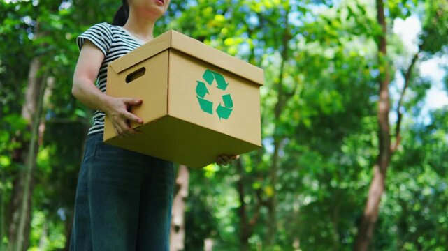 Young Asian woman volunteer holding a recycling box in the park. Concept of recycling, environmental protection, sustainability, zero waste, and ESG strategy on green natural forest background.