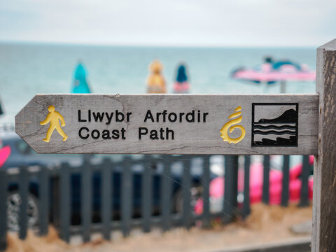 wooden directional sign with graphics and dual language welsh english to coastal path