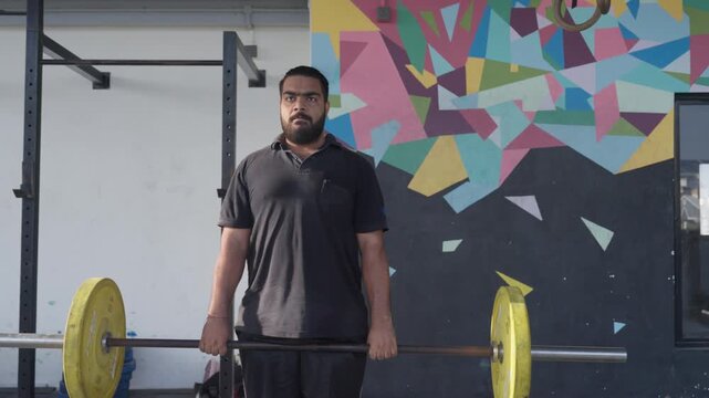 Bearded South Asian male athlete performs a barbell deadlift during functional fitness training in a modern indoor fitness studio. Collection: WORKOUTSERIES2026.
