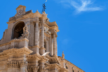Obraz premium the bell tower of Syracuse Cathedral, Sicily, standing out against a clear blue sky, where a seagull can be seen above the cross and a striking cloud that vaguely resembles a large white dove