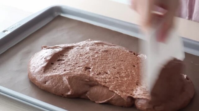 Spreading chocolate cake batter on baking sheet with scraper