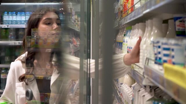 A Young Woman Navigates the Refrigerated Aisle of a Convenience Store, Choosing Between Beverages with Careful Consideration and a Stylish Green Bag