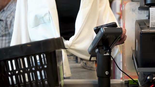 Checkout Scene: A Close-Up of a Customer's Attire at a Payment Counter with Shopping Basket and Digital Payment Device in Focus