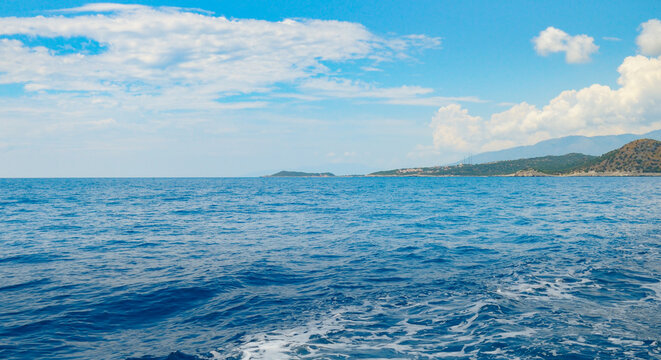 Scenic view of deep blue sea water with coastal mountains in distance. Tranquil turquoise sea horizon under a partly cloudy sky with copy space.