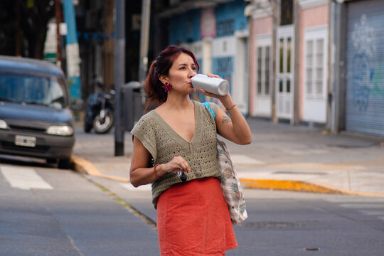 Latina woman crossing street and drinking water