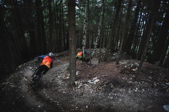 Two mountain bikers riding enduro bikes through a bike park trail,