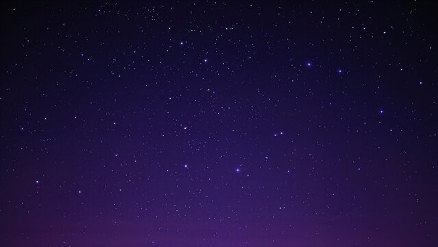 A clear night sky filled with stars seen against a dark purple background.