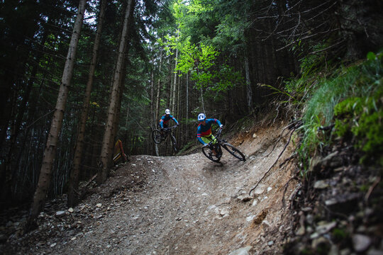 Two mountain bikers riding enduro bikes through a bike park trail,