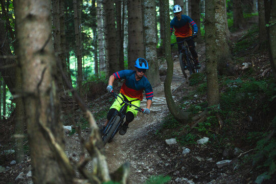 Two mountain bikers riding enduro bikes through a bike park trail,