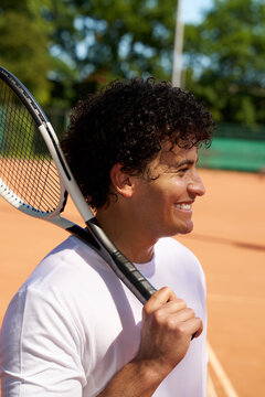Smiling Man Holds Tennis Racket on Court During Sunny Day