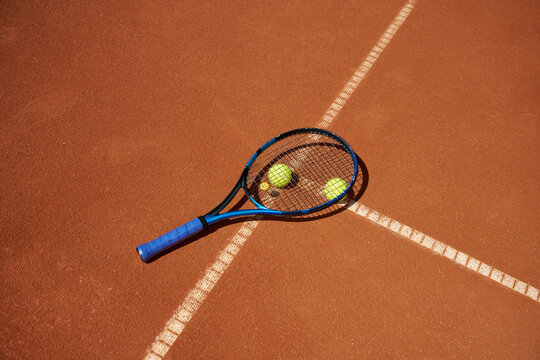 Tennis Racket and Balls on Clay Court During a Sunny Day