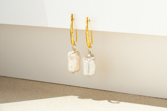 Gold Earrings with Baroque Pearl Charm Hanging on White Paper