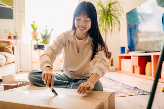 A woman opening a box sitting on the floor