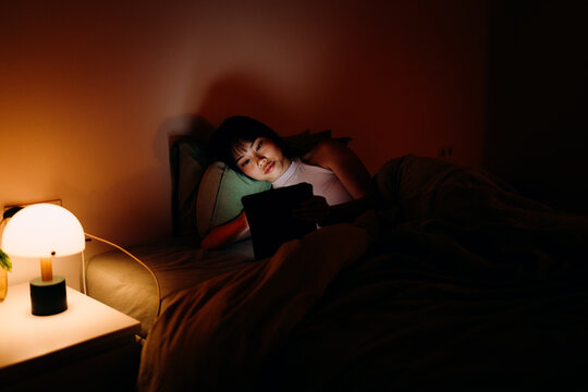 A woman uses a tablet in the bed at night