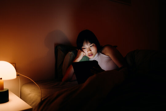 A woman uses a tablet in the bed at night