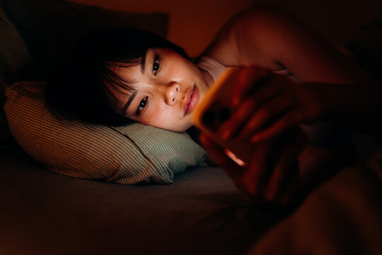 A woman uses a mobile phone in the bed at night
