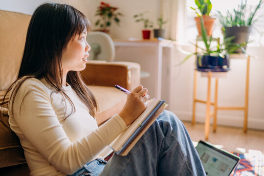 A woman writing in a notebook sitting on the floor