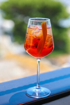 A bright orange Aperol spritz cocktail with ice and citrus peel served outdoors in sunlight.
