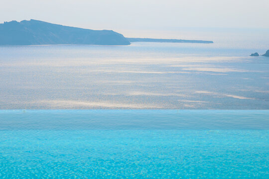 A tranquil view of the sea and horizon beyond a turquoise infinity pool under soft daylight in Santorini, Greece.