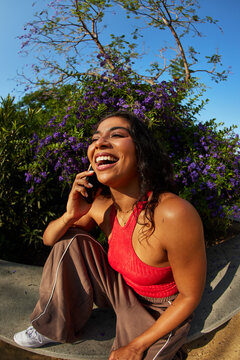 Smiling woman talks on the phone in a garden during the day
