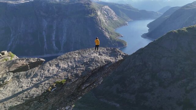 Odda, Norway - 19.07.2026: Drone view of lone hiker on Trolltunga rock ledge overlooking Ringedalsvatnet lake and steep mountain valley.