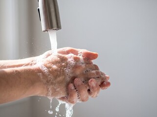 Fototapeta premium Close-up of a person's hands being thoroughly washed with soap and water under a running faucet, creating lather.