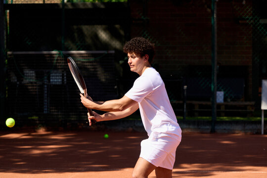 Young Man Practices Tennis on Outdoor Court During Sunny Day