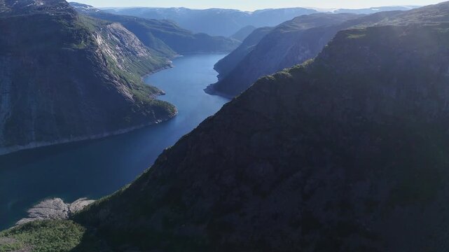 Drone perspective over deep Norwegian fjord, rugged mountains, and rocky plateau near Trolltunga in summer light.