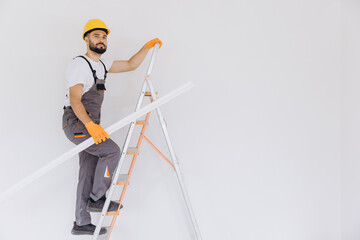 Handyman in safety gear on a ladder holding trim, preparing for home renovation and interior construction work © anatoliycherkas