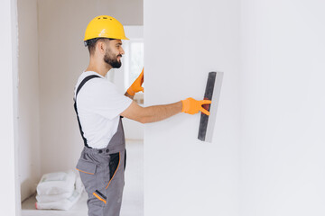 Naklejka premium Manual worker plastering a wall in a room during home renovation, preparing surface finish for painting