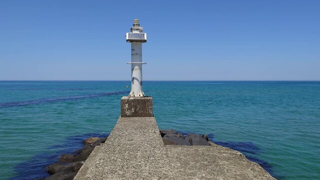 Concrete jetty with small white lighthouse extending into clear blue sea at Aoya coast, Tottori, Japan