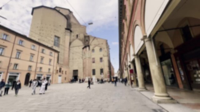 Anonymous blurred people enjoying a sunny day, walking along the historic porticoes and medieval buildings in the famous Piazza Santo Stefano, one of the main landmarks of Bologna, Italy
