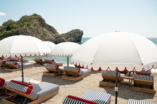 Luxury sunbeds with thick mattresses in blue and white stripes on an idyllic private sand beach in Mazzar&ograve;, Sicily on hot summer day