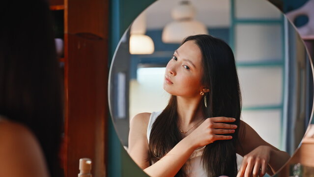 Asian woman brushing long hair in mirror. Close up beauty hair care routine.