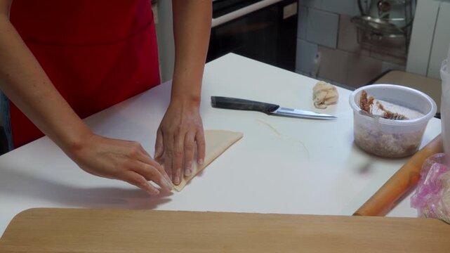 A woman folds dough over meat filling on a white table in the kitchen. She feels focused, passionate, and satisfied during her cozy afternoon cooking routine.