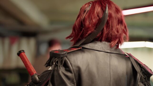 Mysterious woman with short red hair in a futuristic combat costume walking slowly through a dimly lit underground location, showcasing her detailed armor and swords from behind in slow motion