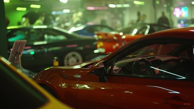 Custom and vintage cars lined at an auto show, people admiring shiny modified and classic vehicles under green and purple neon lights, capturing lively exhibition vibes