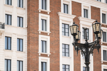 Obraz premium Decorative street lamp post with wrought iron elements installed on a city street in front of modern architecture.
