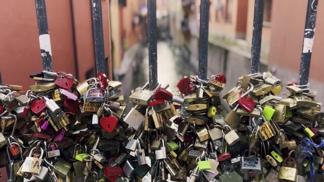 Romantic love padlocks attached to a metal railing on a bridge over a canal in Bologna, Italy, symbolizing eternal love and commitment with many colorful heart-shaped locks from lovers