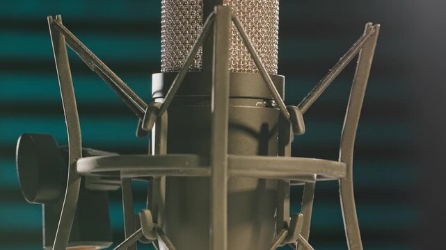Slow motion colorful studio shot of voiceover dialogue podcast microphone on stand in close-up detail with acoustic foam in recording space with dark background and bright lighting of broadcast vo mic