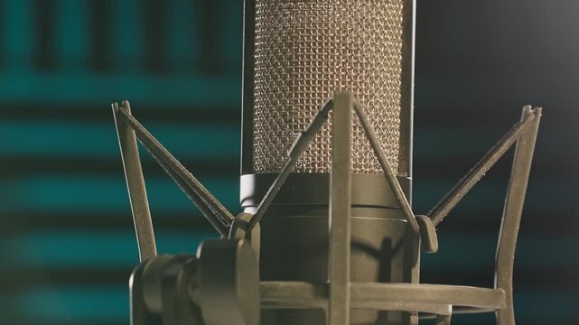Slow motion colorful studio shot of voiceover dialogue podcast microphone on stand in close-up detail with acoustic foam in recording space with dark background and bright lighting of broadcast vo mic