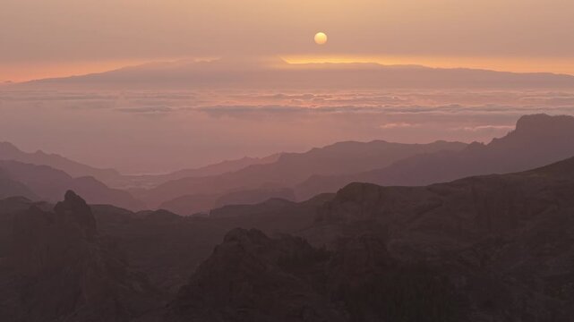 Beautiful aerial view of the sun setting over the layered mountains of Gran Canaria, with the Teide volcano visible in the distance